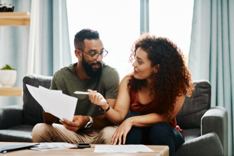 Couple sitting on couch reviewing homeownership costs and budgeting; financial planning for first-time home buyers.