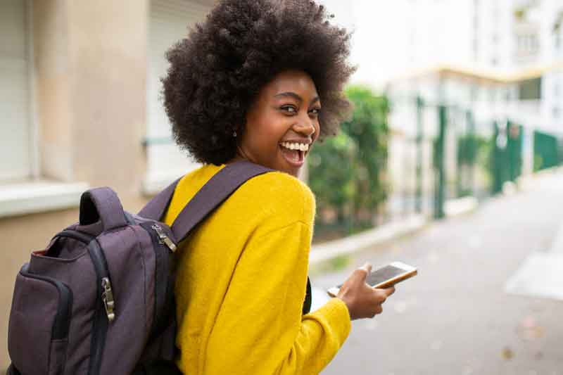 College student with a bookbag smiling while walking, holding a phone, representing education tax benefits and smart savings for students.