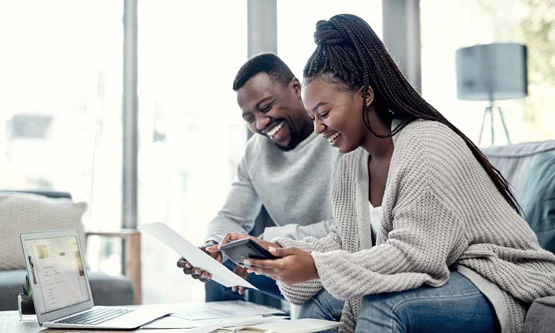 Happy couple reviewing tax planning strategies with papers, a calculator, and laptop to save money and optimize their tax savings.