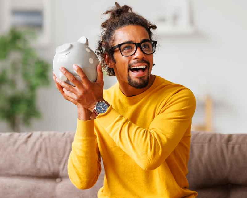 Smiling man holding a piggy bank, ready to file taxes now and pay later with a refund transfer.