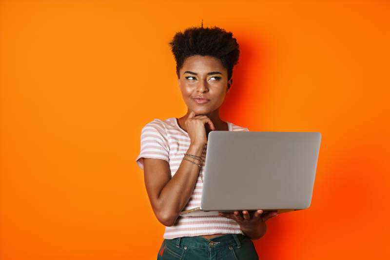 A woman holding her laptop and thoughtfully considering options, possibly evaluating the differences between an HSA and FSA for tax advantages.
