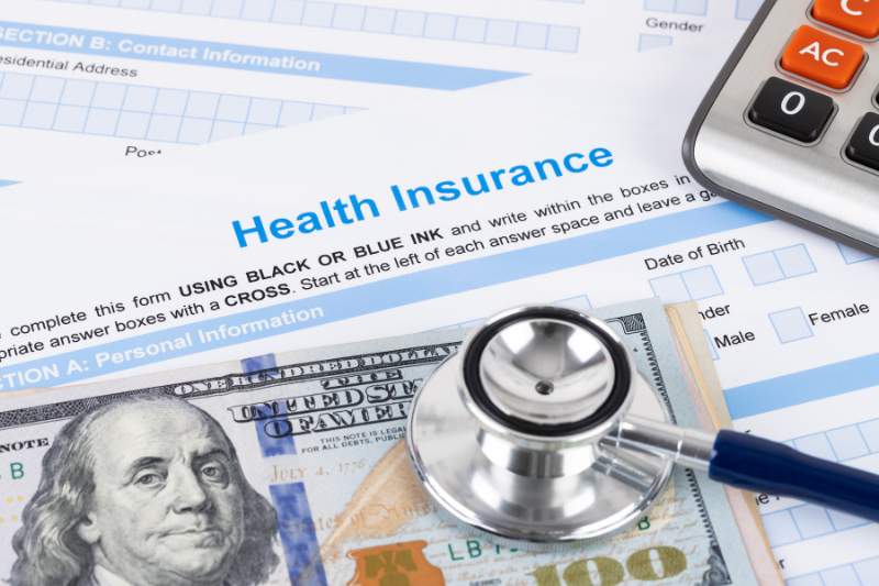 Health insurance paperwork, calculator, and cash illustrating the potential tax deductions for insurance premiums.