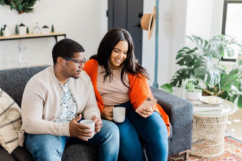 Couple reviewing tax tips for married filing jointly on a smartphone while sitting on a sofa, planning their tax return.