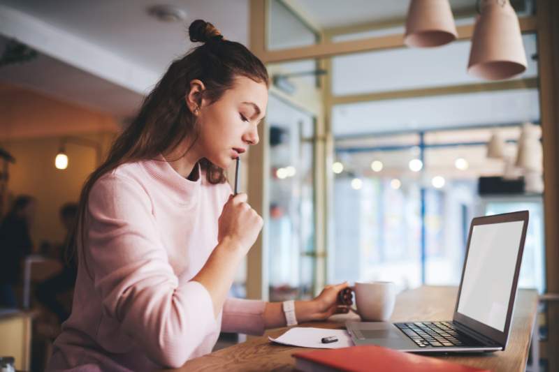 Young woman thinking while using her laptop, researching the difference between net income and gross income for personal finance planning.