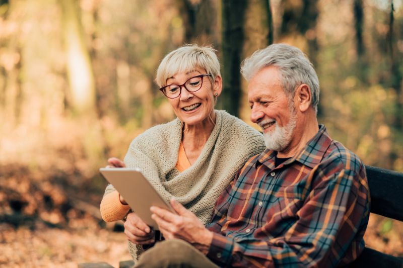 Happy senior couple reviewing their retirement account and RMD calculation on a tablet outdoors