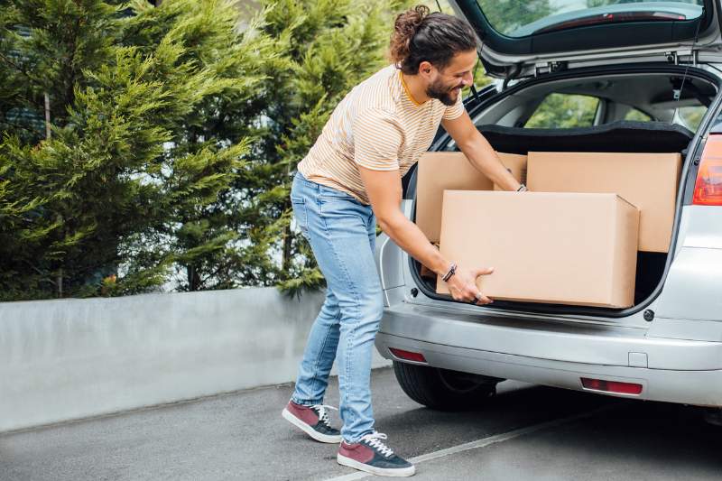Man loading moving boxes into his car, representing deductible moving expenses and tax-saving tips for relocations.