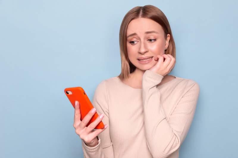 Nervous woman looking at her phone worried about filing taxes late and missing the IRS deadline.